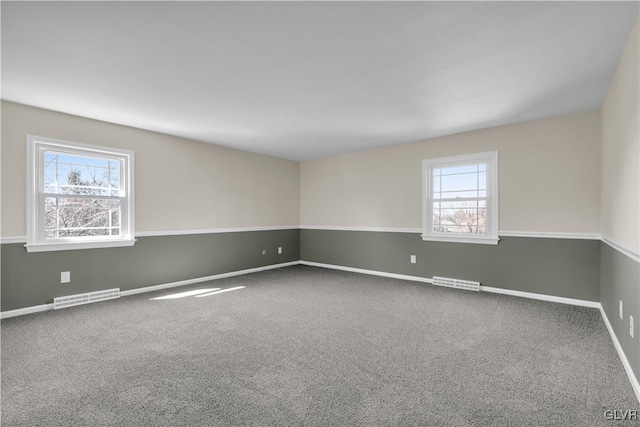 carpeted spare room featuring a wealth of natural light, visible vents, and baseboards