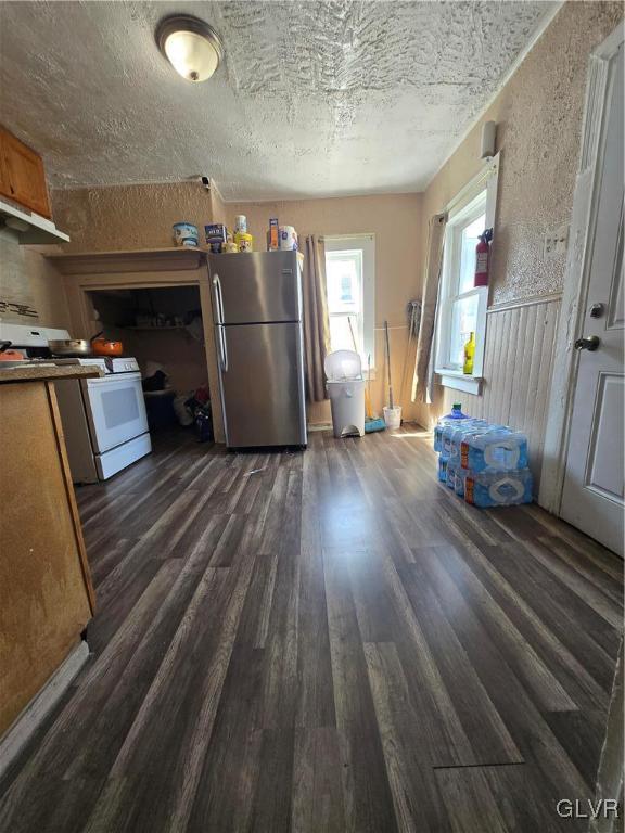 kitchen featuring dark wood finished floors, white range oven, wainscoting, freestanding refrigerator, and a textured ceiling