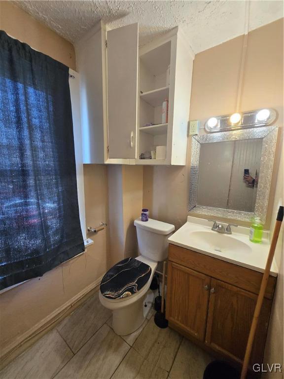 half bath featuring a textured ceiling, vanity, and toilet