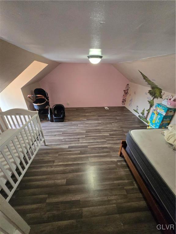 unfurnished bedroom with a textured ceiling, lofted ceiling, and wood finished floors