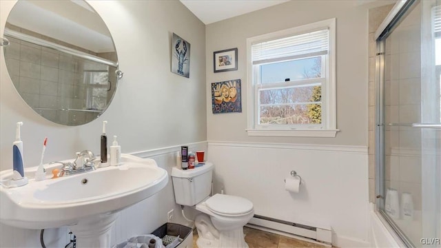 full bathroom featuring a baseboard heating unit, toilet, wainscoting, a shower with shower door, and a sink