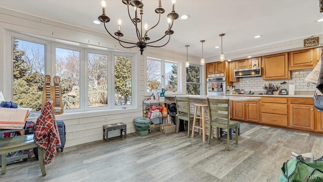 kitchen with tasteful backsplash, ventilation hood, light wood-style floors, light countertops, and stainless steel oven