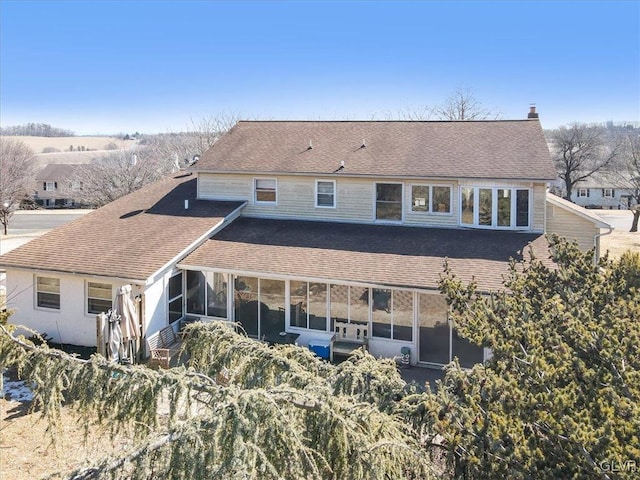 rear view of property with a shingled roof, a chimney, and a sunroom