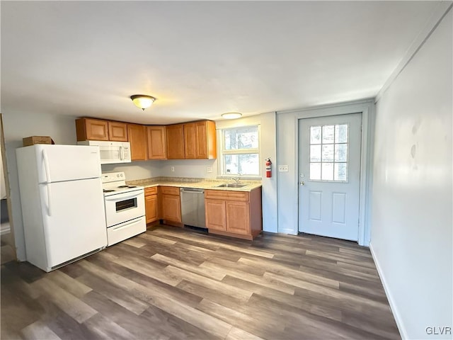 kitchen with white appliances, wood finished floors, baseboards, a sink, and light countertops