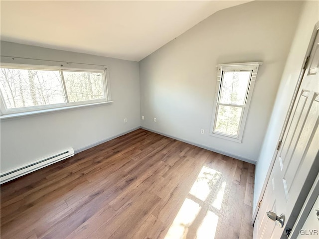 unfurnished bedroom with a baseboard radiator, multiple windows, wood finished floors, and vaulted ceiling