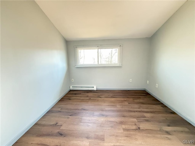 unfurnished room with vaulted ceiling, wood finished floors, baseboards, and a baseboard radiator