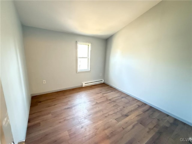 unfurnished room featuring a baseboard heating unit, baseboards, and wood finished floors