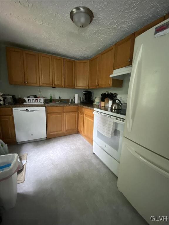 kitchen with brown cabinets, under cabinet range hood, a sink, a textured ceiling, and white appliances