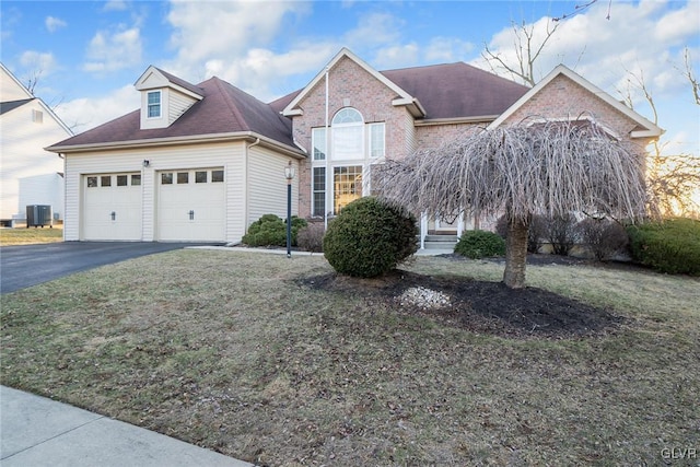 view of front facade featuring a front yard, driveway, an attached garage, central air condition unit, and brick siding