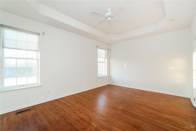 empty room featuring a raised ceiling, wood finished floors, visible vents, and baseboards