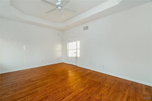 unfurnished room with visible vents, baseboards, a tray ceiling, and wood finished floors