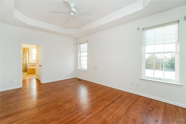 spare room with baseboards, a ceiling fan, a tray ceiling, and wood finished floors