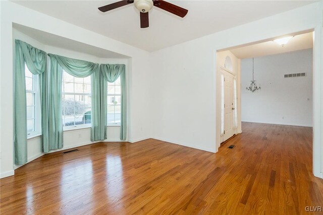 spare room featuring ceiling fan with notable chandelier, wood finished floors, and visible vents