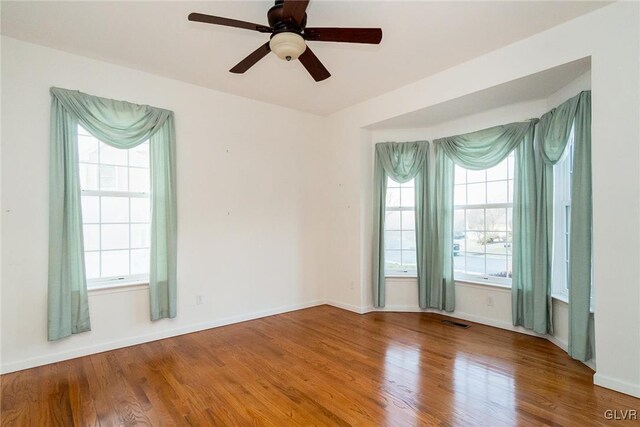 unfurnished room featuring visible vents, a healthy amount of sunlight, baseboards, and wood finished floors