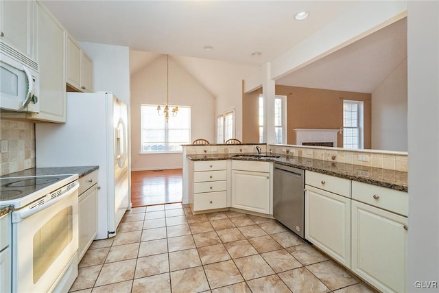 kitchen with a sink, backsplash, white appliances, an inviting chandelier, and lofted ceiling