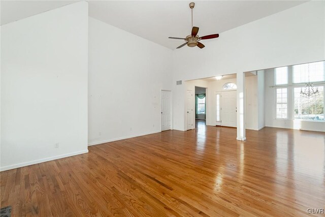 unfurnished living room featuring ceiling fan with notable chandelier, baseboards, light wood-style floors, and a towering ceiling