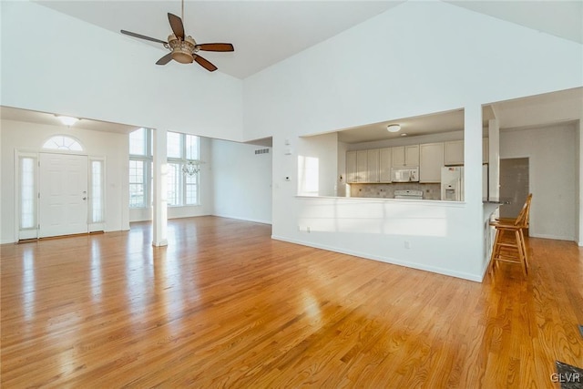 unfurnished living room featuring a high ceiling, a ceiling fan, baseboards, and light wood finished floors