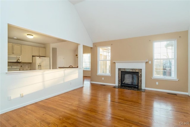 unfurnished living room featuring visible vents, baseboards, a premium fireplace, wood finished floors, and high vaulted ceiling