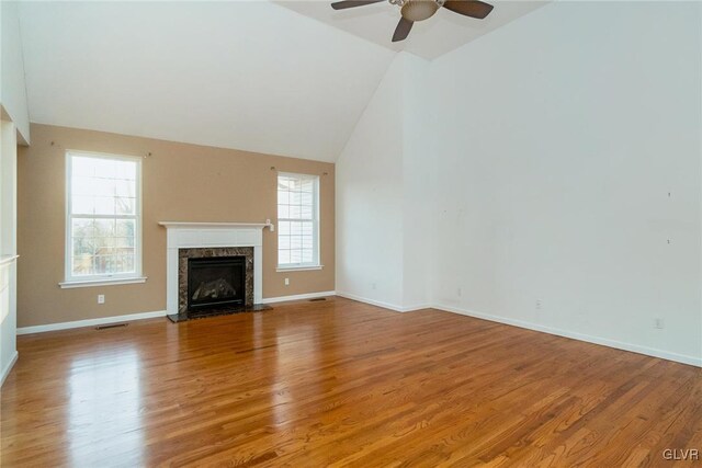 unfurnished living room with a high end fireplace, light wood finished floors, high vaulted ceiling, and baseboards