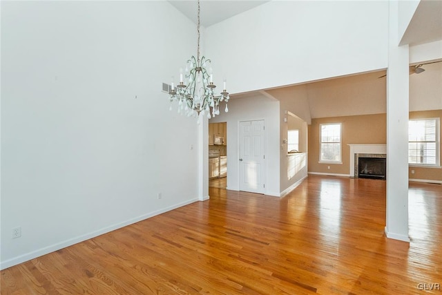 unfurnished living room with visible vents, baseboards, a chandelier, light wood-style flooring, and a fireplace