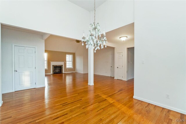 unfurnished living room featuring a premium fireplace, baseboards, high vaulted ceiling, and light wood-style flooring