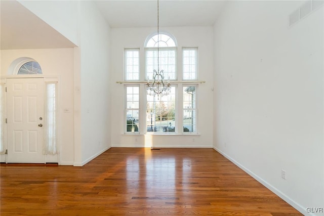 foyer entrance with visible vents, wood finished floors, a high ceiling, baseboards, and a chandelier