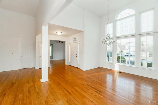 unfurnished room featuring a wealth of natural light, a notable chandelier, a high ceiling, and light wood finished floors