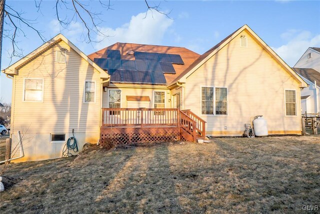 rear view of property featuring a wooden deck, roof mounted solar panels, and a lawn