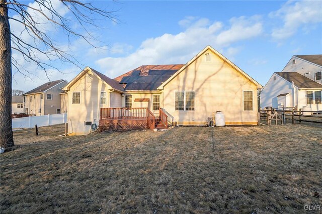 rear view of house with roof mounted solar panels, a lawn, a wooden deck, and a fenced backyard