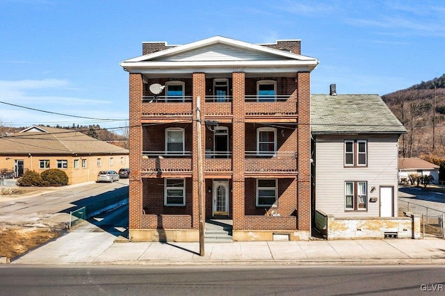 view of front facade with a balcony, brick siding, and a chimney