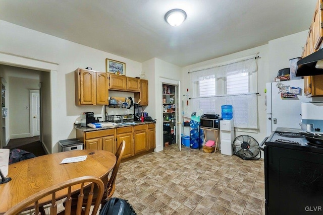 kitchen featuring a sink, brown cabinets, black electric range oven, and freestanding refrigerator