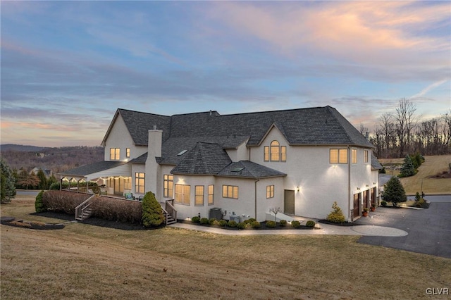 view of front of house featuring a shingled roof, a lawn, stucco siding, a garage, and driveway