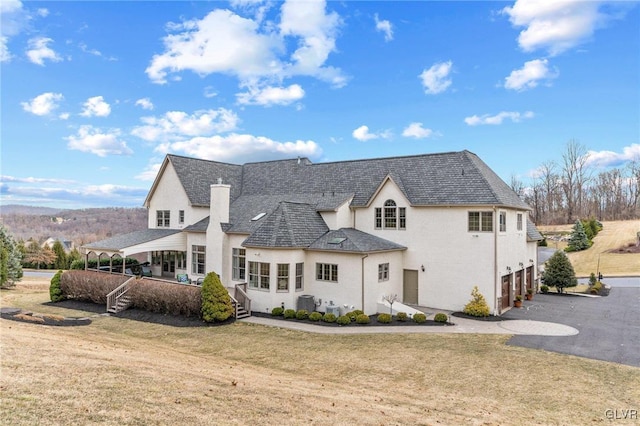 rear view of property with aphalt driveway, an attached garage, a lawn, and stucco siding