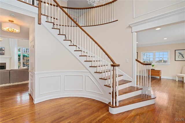 stairs featuring wood finished floors, a fireplace, recessed lighting, ornamental molding, and a decorative wall