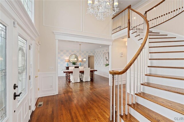 foyer entrance featuring visible vents, ornamental molding, stairway, a decorative wall, and a chandelier