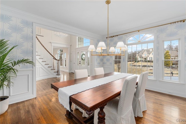 dining room featuring stairway, wood finished floors, wallpapered walls, ornamental molding, and a chandelier