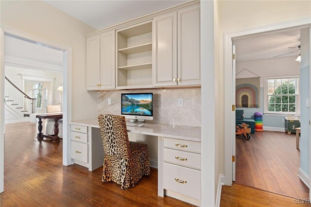 home office featuring baseboards, built in study area, dark wood-type flooring, and a ceiling fan