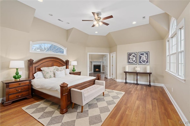 bedroom featuring vaulted ceiling, light wood-style flooring, multiple windows, and baseboards