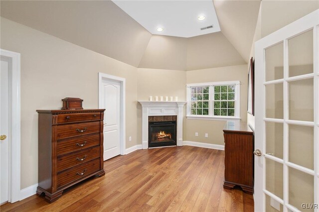 living room featuring visible vents, baseboards, lofted ceiling, a warm lit fireplace, and wood finished floors