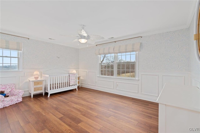 unfurnished bedroom featuring wainscoting, wallpapered walls, crown molding, and wood finished floors