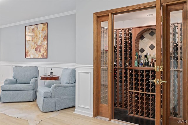 wine area with a decorative wall, a wainscoted wall, crown molding, and wood finished floors