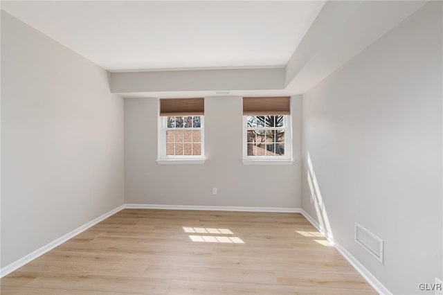 empty room with light wood-style floors, visible vents, and baseboards