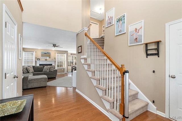 staircase featuring a ceiling fan, wood finished floors, baseboards, and a fireplace