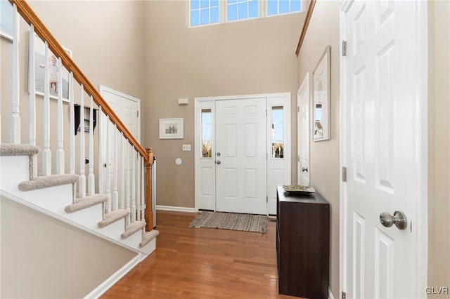 foyer featuring stairway, baseboards, wood finished floors, and a towering ceiling