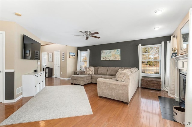 living room with visible vents, a ceiling fan, a glass covered fireplace, light wood finished floors, and baseboards