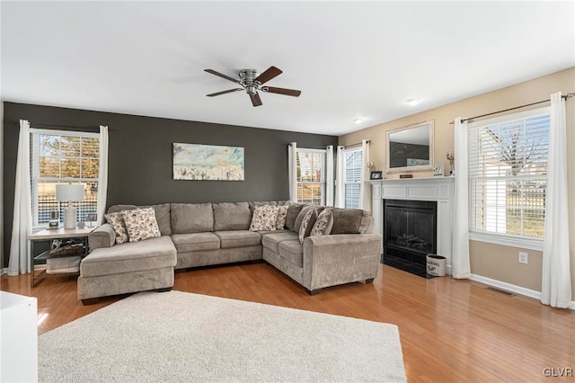 living room featuring a fireplace with flush hearth, light wood-style flooring, visible vents, and a ceiling fan