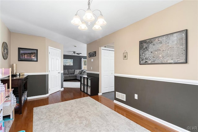 interior space with visible vents, ceiling fan with notable chandelier, dark wood-type flooring, and baseboards