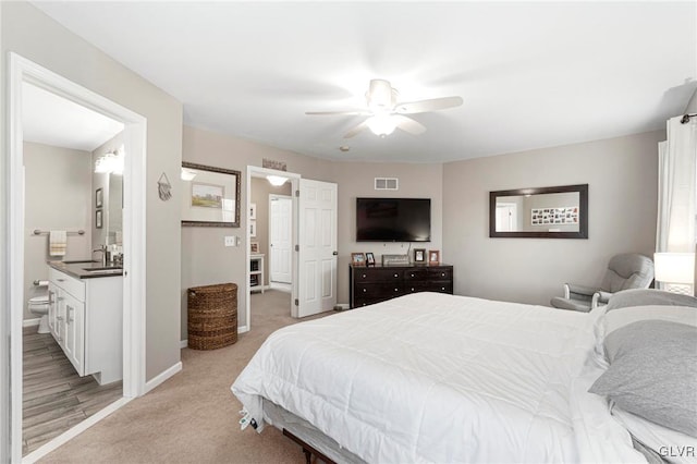 bedroom featuring a ceiling fan, visible vents, baseboards, ensuite bathroom, and light carpet