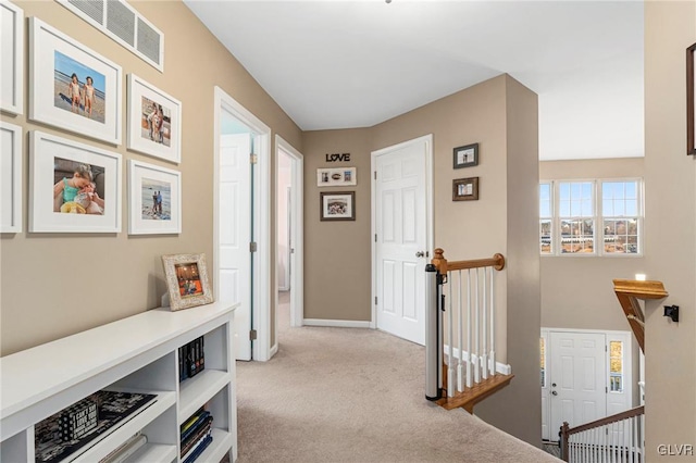 hallway with an upstairs landing, light colored carpet, visible vents, and baseboards