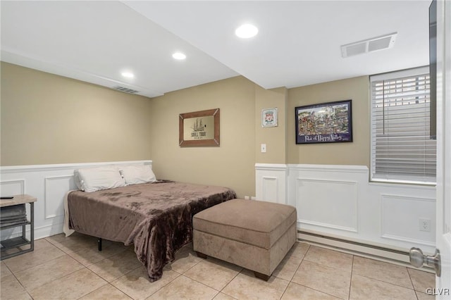 bedroom featuring a baseboard heating unit, a wainscoted wall, light tile patterned floors, and visible vents